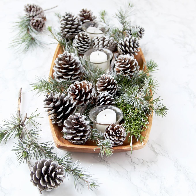 white table decorations with candles and DIY snow covered pine cones & branches in wood tray